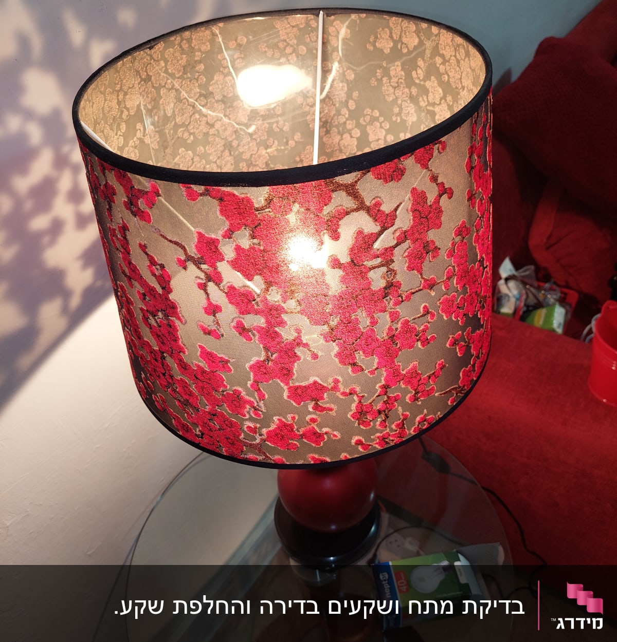 מנורה עם אהיל פרחוני ונורה חשמלית על שולחן זכוכית